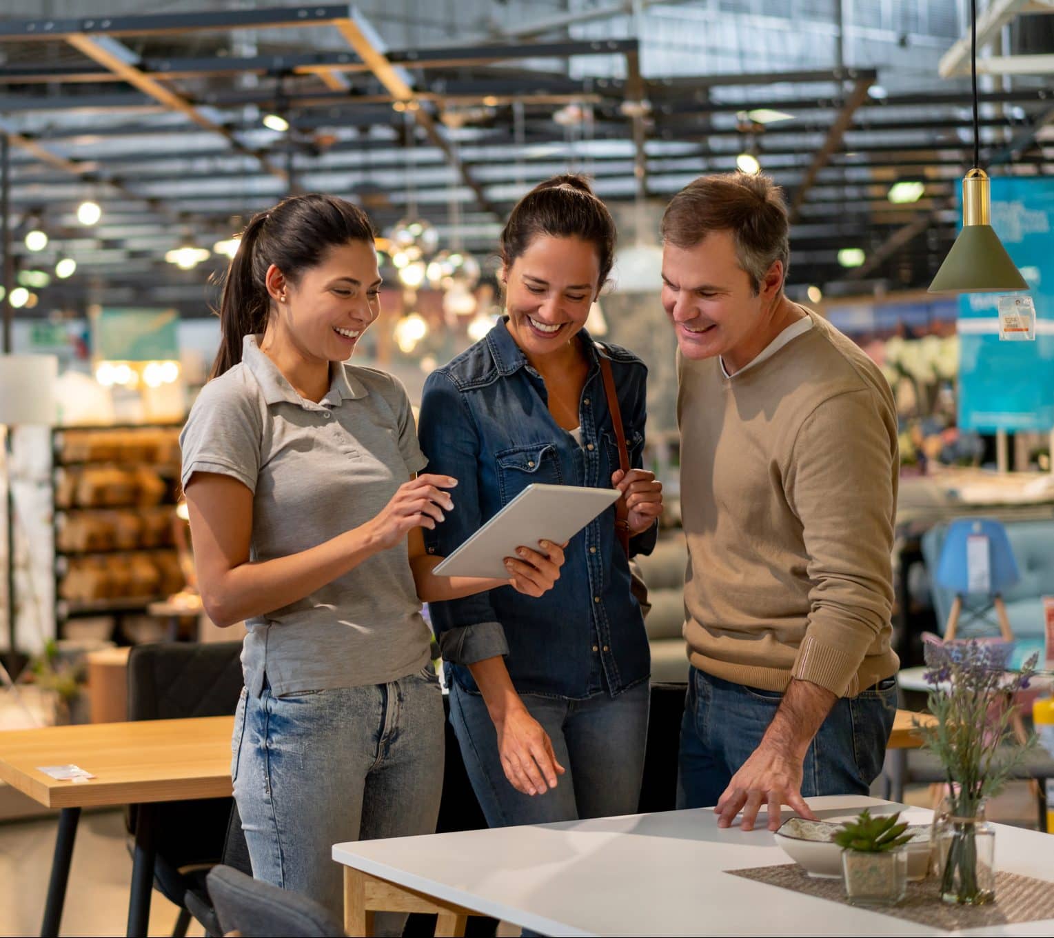 Cheerful sales woman showing a design on tablet to mid adult couple looking for furniture at a home store